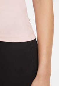 Top ajustado de color rosa claro con una textura suave, combinado con pantalones negros de tiro alto; presenta una pequeña etiqueta "Guess" en la costura lateral.