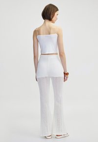 Witte cropped tanktop met dunne bandjes, gecombineerd met witte flare gebreide broeken met opengewerkte patronen en een gestructureerde afwerking.