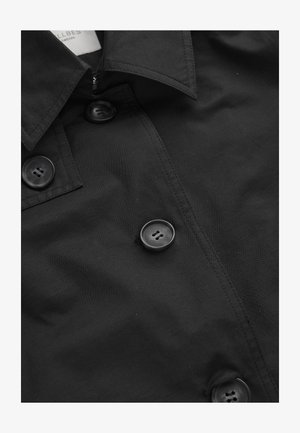 Schwarzes Hemd mit Knöpfen, großen vierlochigen Knöpfen und spitzem Kragen, das detaillierte Nähte und Stoffstruktur zeigt.