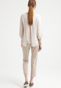 Lys beige bluse med scoop-udskæring, ¾ ærmer og slids bagpå. Parret med slanke lys beige bukser og grå slip-on sko.