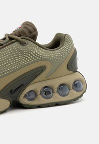 Olivgrön sneaker med mesh-övre, strukturerade detaljer, vadderad krage och unika luftdämpande poddar i transparent material på sulan.