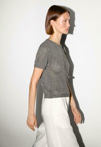 Gray knitted short-sleeve top with a round neck, paired with white linen trousers. Texture appears lightweight and breathable.