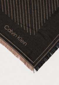 Mustad ja pruunid Calvin Kleini sallinurgad vertikaalsete joontega, soonitud ääred ning brändi nimi kudumisega piiri lähedal valge tausta peal.