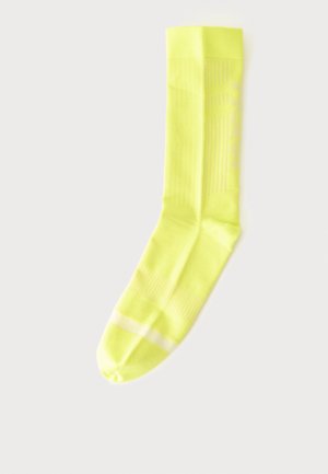 Chaussette d'équipage jaune vif unique avec une texture côtelée subtile et une fine bande blanche horizontale près des orteils sur un fond uni.