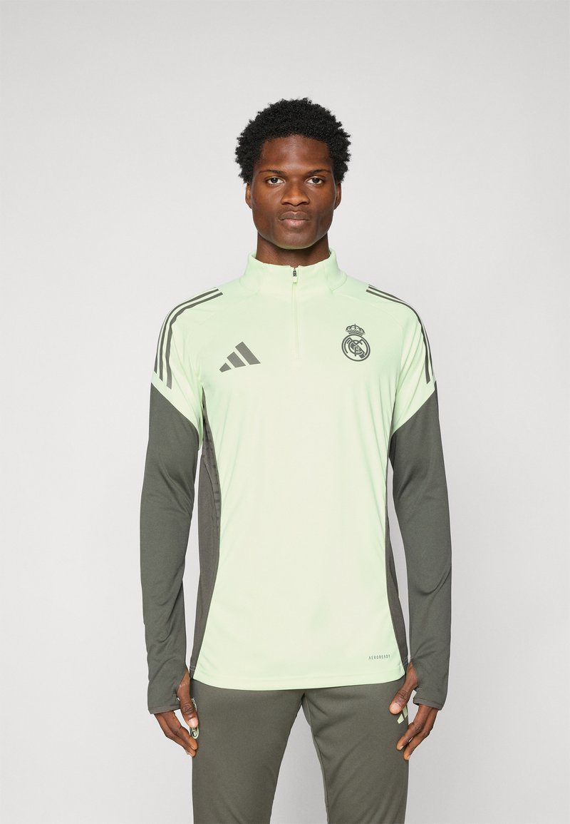 Hellgrüner Sportpullover mit langen Ärmeln, Reißverschlusskragen und dunkelgrauen Akzenten. Mit Adidas- und Real Madrid-Logos. Weicher Stoff.