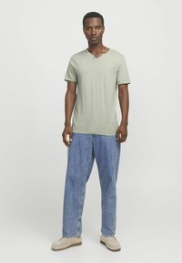 Lysgrøn kortærmet T-shirt med V-hals og knapdetalje, parret med løse blå denimjeans og beige slip-on sko.