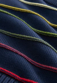 Marineblauer Strickstoff mit horizontalen Streifen in Grün, Gelb und Rot. Glatte Textur mit sichtbaren Stichtdetails.