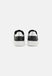 Zapatillas negras y plateadas con un cuerpo texturizado negro, acentos plateados lisos y suelas de goma blanca. Diseñadas con un perfil bajo y estilo sin cordones.