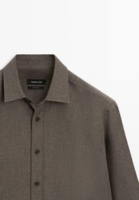 Mørkegrå skjorte med knapper, lavet af et struktureret stof, med klassisk krave og sorte knapper. Har mærkater inde i kraven.