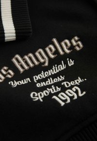 Black fabric sweatshirt featuring white and cream embroidery. Text reads "Los Angeles," "Your potential is endless," "Sports Dept," and "1992."