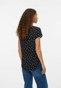 Zwarte top met korte mouwen, voorzien van witte stippen, een gebogen zoom en een ontspannen pasvorm, gecombineerd met lichtblauwe wijde jeans.