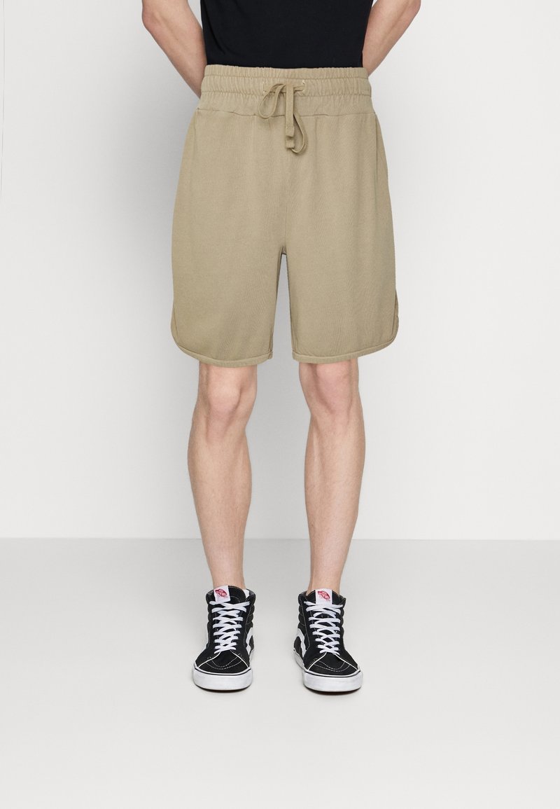 Pantalones cortos deportivos color caqui con cintura elástica y cordón. Presenta bolsillos laterales y una textura suave. Combinados con zapatillas altas negras.