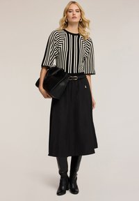Suéter de punto a rayas blancas y negras con escote redondo, combinado con una falda negra, cinturón negro y botas negras elegantes, sujetando un bolso negro.