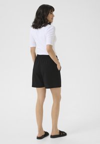 Shorts noirs texturés, en tissu, arrivant aux genoux avec une taille élastique et des poches latérales, portés avec un haut blanc ajusté et des sandales.
