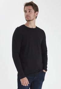 Sort langærmet t-shirt med rund hals i blødt stof, parret med mørkeblå jeans. Har en tætsiddende pasform og en udekoreret stil.