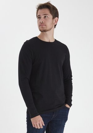 Black long-sleeve round-neck t-shirt made of soft fabric, paired with dark blue jeans. Features a fitted design and unembellished style.