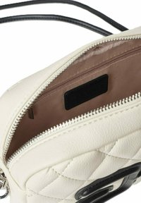 Piccola borsa a tracolla in pelle bianca trapuntata con cerniera argentata, interno in tessuto beige e dettaglio in pelle nera con logo sul fronte.