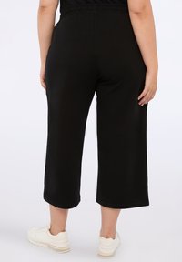 Černé culottes kalhoty vyrobené z měkké tkaniny, s elastickým pasem a zkrácenou délkou, kombinované s bílými teniskami.