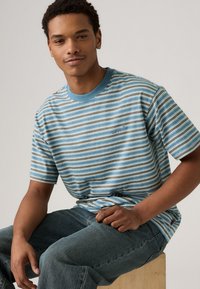 Short-sleeve striped t-shirt in teal, beige, and white. Fabric has a soft texture; features a crew neck and small logo on chest.