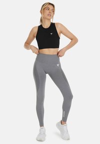 Zwarte crop top met een ronde hals, gecombineerd met grijze high-waisted leggings met een zijpaneelontwerp en witte logo-accenten. Witte sneakers.