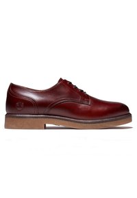 Chaussure derby en cuir verni bordeaux pour homme avec semelle en caoutchouc marron et logo embossé près du talon, vue de côté.