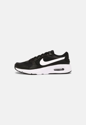 Sort-hvid Nike Air Max sneaker set fra siden med synlig luft pude i den hvide sål mod en ensfarvet baggrund.