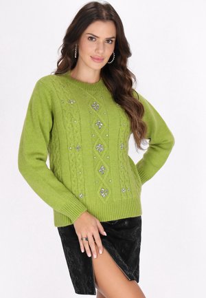 Zöld cable-knit pulóver, világos virágmintákkal díszítve és kerek nyakkivágással, fekete texturált szoknyával párosítva, oldalra cipzárral.