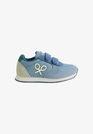 Zapato deportivo de color azul claro con paneles de ante y malla, correas de velcro y un logo decorativo. Presenta una suela texturizada y una plantilla suave.