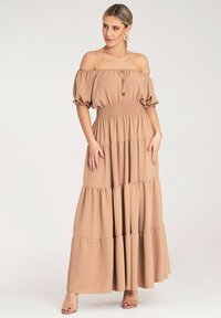 Maxi sukienka z odkrytymi ramionami w kolorze beżowym, z marszczoną talią, balonowymi rękawami oraz warstwowym krojem z drewnianymi guzikami.