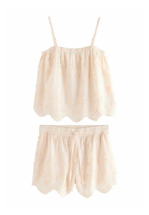Krämfärgad ärmlös topp och matchande shorts med broderade blommönster och vågiga kanter.
