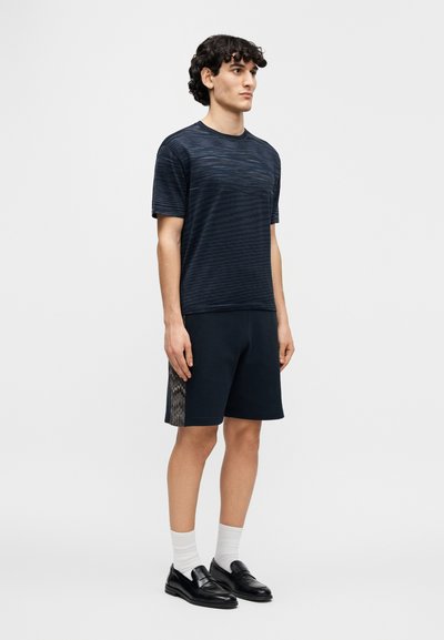 Μπλούζα με ναυτικές ρίγες σε συνδυασμό με σκούρο σορτς που έχει πλευρική πάνελ με υφή και σχέδιο. Φοριέται με λευκές κάλτσες και μαύρα loafers.