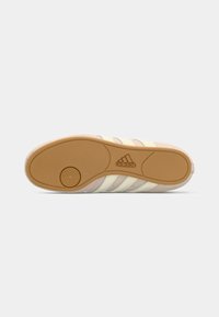 Beige Adidas sporta apavu zole ar gumijas ārējo zoli, apļa protektora raksts tuvu papēdim un Adidas logo centrā.
