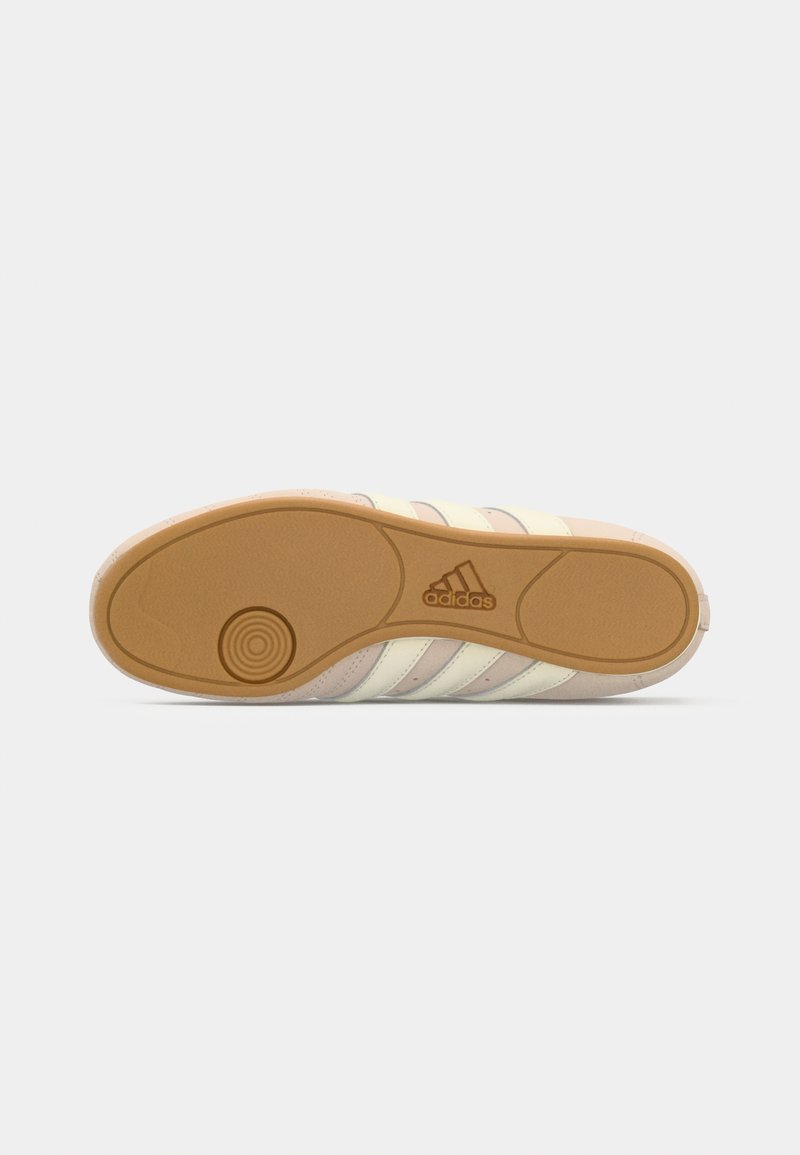Suela de zapatilla Adidas beige con suela de goma, patrón de tracción circular cerca del talón y logo de Adidas en el centro.
