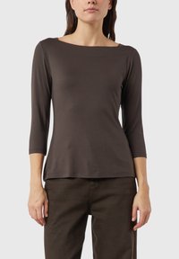 Ciemnobrązowa dopasowana bluzka z długim rękawem, szerokim dekoltem, gładką fakturą i rękawami o długości do ¾, w połączeniu z ciemnymi spodniami.