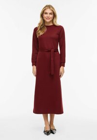 Bordowa sukienka z długim rękawem i paskiem w talii, wykonana z prążkowanej tkaniny, o prostym kroju i zaokrąglonym dekolcie.