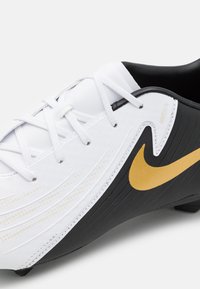 Vitt och svart fotbollssko med texturerad design, utrustad med en gyllene Nike-swoosh, snören och en framträdande böjd form.