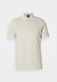 Polo beige avec une patte de boutonnage à deux boutons, col blanc et accents sur les manches, arborant une subtile étiquette logo sur la poitrine, texture en coton lisse.