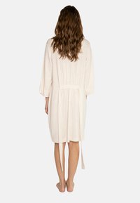 Robe di colore crema lunghezza ginocchio con maniche a tre quarti, vita arricciata e una cintura sul retro. Materiale morbido e testurizzato.