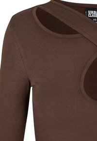 Brown long-sleeve top with a ribbed texture, featuring a circular cutout and cross-body straps for a unique design.