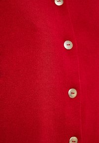 Rode gebreide cardigan met een rij metalen knopen aan de voorkant. Zachte textuur met geribbelde details.