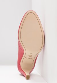 Chaussure rouge à talons hauts présentée semelle vers le haut, montrant une semelle beige lisse avec la pointure 37 et le nom de la marque "Tamaris".