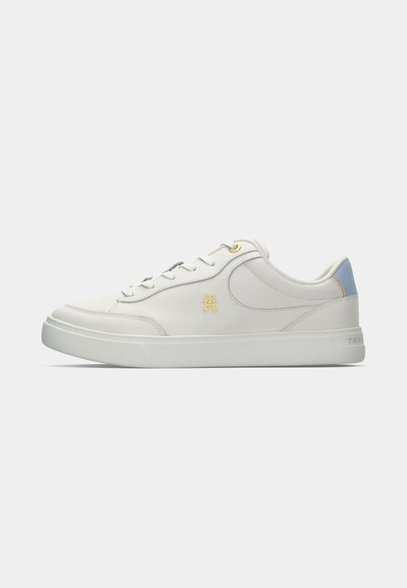 Weiße Low-Top-Sneaker mit goldenen Ösen und Logo, blauer Fersenlasche, Schnürdesign und dicker weißer Sohle auf einfarbigem Hintergrund.