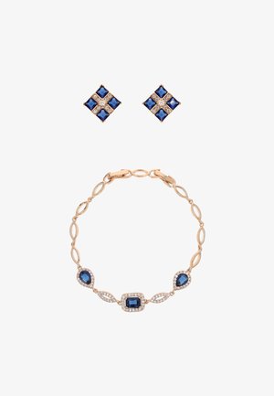 Set di gioielli in tonalità oro con orecchini con gemme blu impreziositi da diamanti e un braccialetto con maglie ovali e varie pietre blu.