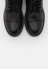 Svarta läderstövlar med rund tå, med en slät yta, snörningsdesign och subtila sömnadsdetaljer, mot en vit bakgrund.