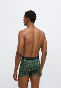 Zelene boksarice z vzorcem in črnim pasom z napisom BJÖRN BORG. Material je videti gladek in tesno prilegajoč, z jasno vidnim cik-cak vzorcem.