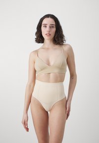 Beige saumaton rintaliivisetti ja korkeavyötäröiset alushousut. Pehmeä rakenne ohuilla olkaimilla ja V-päätteisellä muotoilulla. Minimalistinen tyyli ilman kuvioita tai yksityiskohtia.