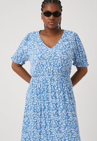 Μπλε φλοράλ φόρεμα με λευκά σχέδια, V-λαιμόκοψη, κοντά φουσκωτά μανίκια και ελαστική μέση. Λείος ύφασμα με χαλαρή εφαρμογή.