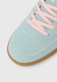 Μύτη αθλητικού παπουτσιού από σουέντ σε ανοιχτό μπλε χρώμα με ροζ κορδόνια και καφέ λαστιχένια σόλα σε λευκό φόντο.