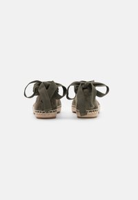 Espadrilles en daim vert avec des liens en tissu, dotées d'une semelle en jute tissée et de détails cousus autour du bord.