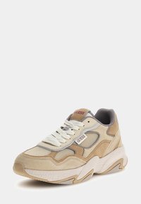 Baskets en mesh beige et marron clair avec des accents gris, semelle blanche épaisse, et logo "GUESS" bien visible sur le côté et la languette. Design classique à lacets.